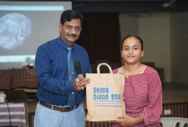 Dr. Prakash H. Kurmi presenting a certificate to a student during the Diabetes Awareness Program at Smt. Laxmiben & Shree Chimanlal Mehta Arts College organized by Shivam Charitable Trust.